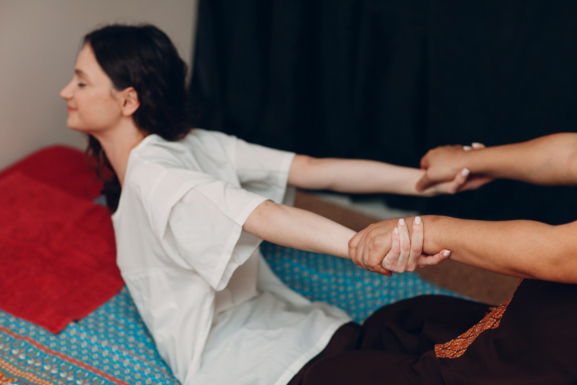 Thai man making classical thai massage procedure to young woman at beauty spa salon